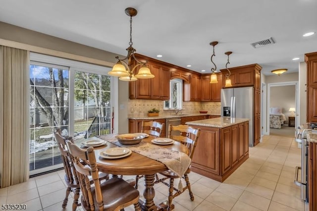 kitchen featuring a kitchen island, decorative light fixtures, stainless steel fridge, decorative backsplash, and light stone countertops