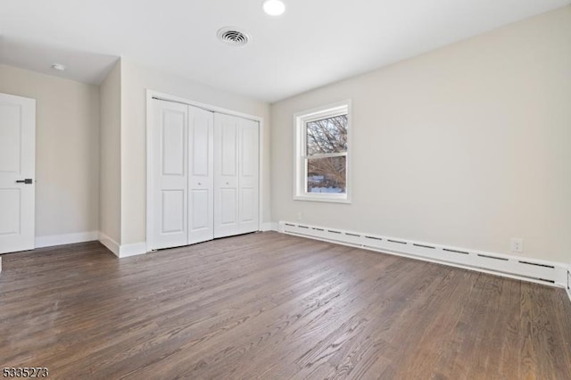 unfurnished bedroom with baseboard heating, dark hardwood / wood-style floors, and a closet