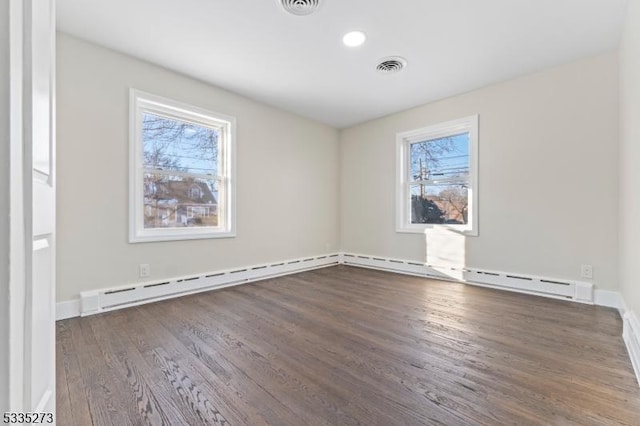 empty room featuring dark hardwood / wood-style floors, a wealth of natural light, and baseboard heating