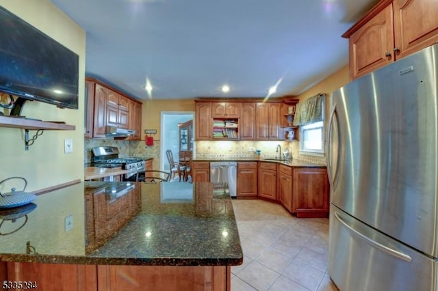 kitchen featuring appliances with stainless steel finishes, light tile patterned floors, decorative backsplash, and dark stone countertops