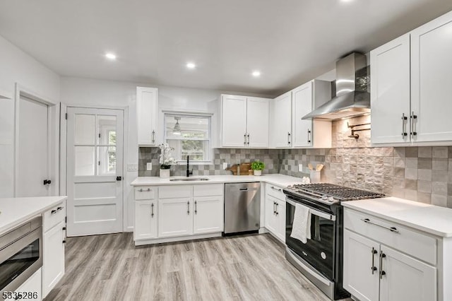 kitchen featuring appliances with stainless steel finishes, sink, white cabinets, decorative backsplash, and wall chimney exhaust hood