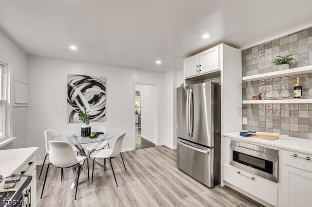 kitchen featuring appliances with stainless steel finishes, white cabinets, light wood-type flooring, and decorative backsplash