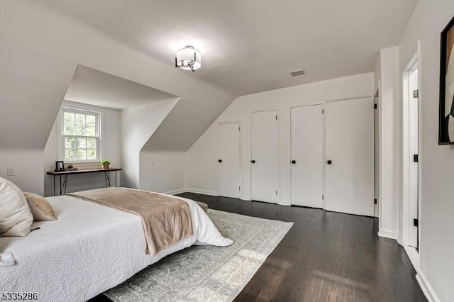 bedroom with multiple closets, vaulted ceiling, and dark wood-type flooring