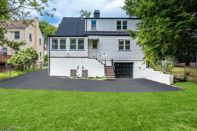 rear view of property featuring a garage, a yard, and central AC unit