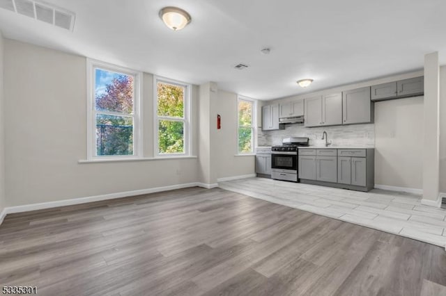 kitchen featuring sink, light hardwood / wood-style flooring, gray cabinetry, backsplash, and stainless steel gas range oven