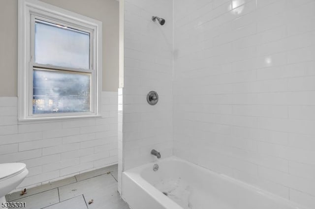 bathroom featuring tile walls, tiled shower / bath, tile patterned floors, and toilet