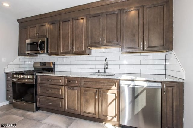 kitchen with sink, backsplash, light stone countertops, and appliances with stainless steel finishes