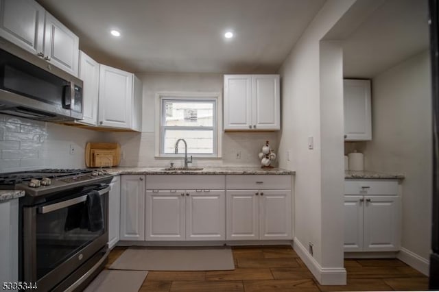 kitchen with appliances with stainless steel finishes, sink, white cabinets, and light stone counters