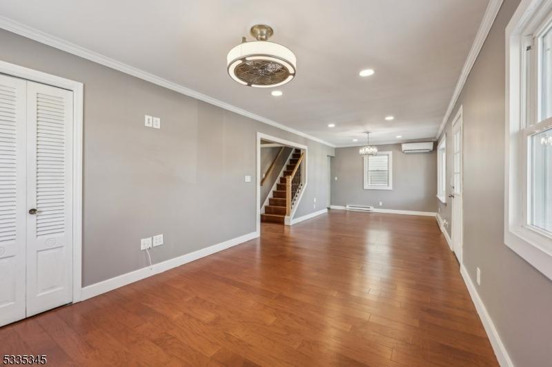 unfurnished living room with an AC wall unit, hardwood / wood-style floors, a chandelier, a baseboard heating unit, and crown molding