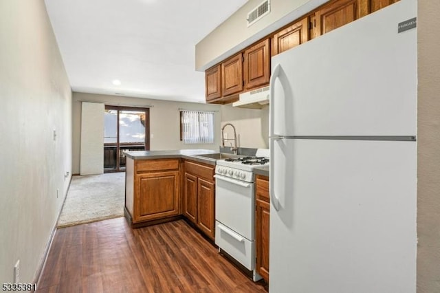 kitchen with dark hardwood / wood-style flooring, sink, white appliances, and kitchen peninsula