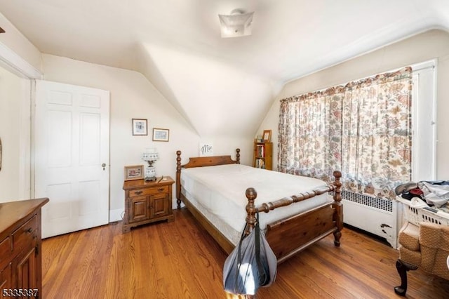 bedroom featuring radiator heating unit, vaulted ceiling, and light hardwood / wood-style flooring