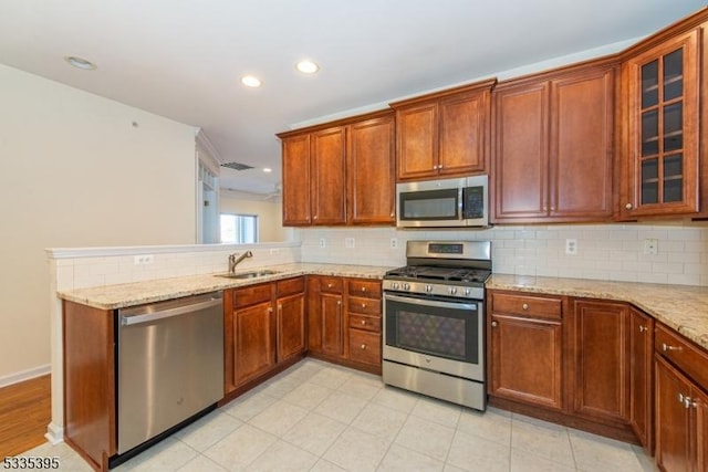 kitchen with sink, decorative backsplash, stainless steel appliances, and light stone countertops