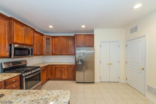 kitchen with tasteful backsplash, light tile patterned flooring, light stone countertops, and appliances with stainless steel finishes