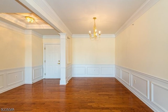 spare room featuring decorative columns, ornamental molding, dark wood-type flooring, and a chandelier