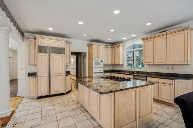 kitchen with light brown cabinetry, built in appliances, a kitchen island, dark stone counters, and decorative columns