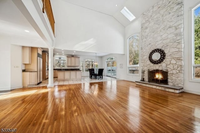 unfurnished living room with ornate columns, a stone fireplace, high vaulted ceiling, and light hardwood / wood-style floors