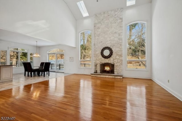 unfurnished living room featuring a stone fireplace, an inviting chandelier, a skylight, high vaulted ceiling, and light hardwood / wood-style floors