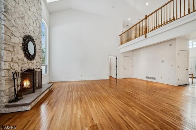 unfurnished living room with plenty of natural light, wood-type flooring, a stone fireplace, and a high ceiling