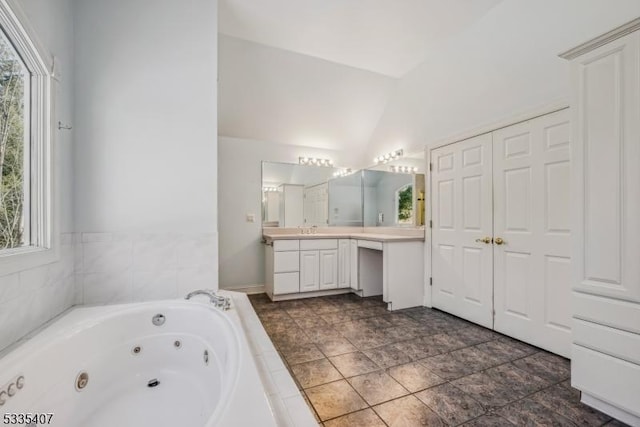 bathroom with a relaxing tiled tub, lofted ceiling, and vanity