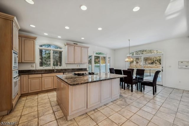 kitchen featuring light brown cabinetry, decorative light fixtures, a kitchen island, dark stone counters, and oven