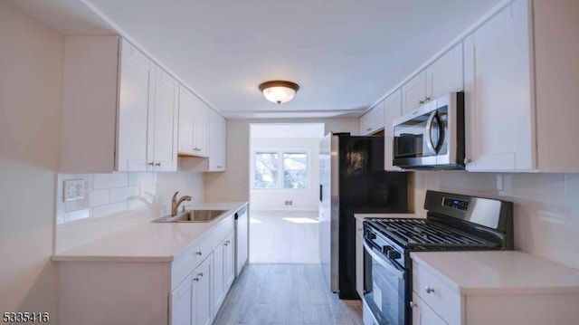 kitchen with sink, white cabinets, decorative backsplash, light hardwood / wood-style floors, and stainless steel appliances