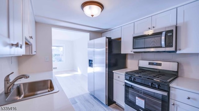 kitchen with sink, light wood-type flooring, white cabinets, stainless steel appliances, and backsplash