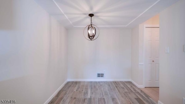 empty room featuring a chandelier and light hardwood / wood-style floors