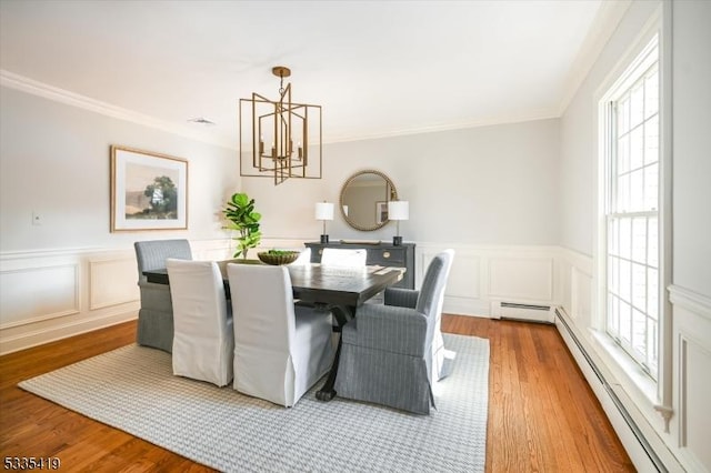 dining space featuring a baseboard radiator, ornamental molding, a notable chandelier, and light wood-type flooring