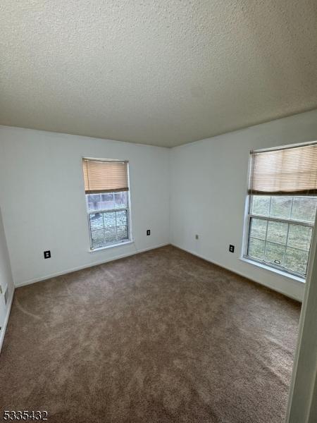 unfurnished room with plenty of natural light, a textured ceiling, and dark carpet