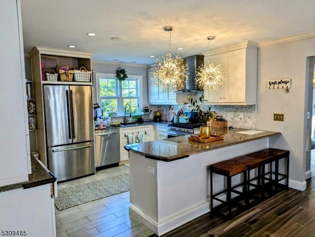 kitchen with white cabinetry, decorative light fixtures, appliances with stainless steel finishes, kitchen peninsula, and wall chimney range hood