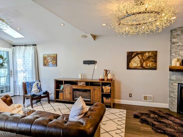 living room with a notable chandelier, lofted ceiling with skylight, a fireplace, and light wood-type flooring