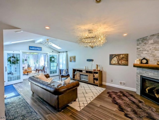 living room featuring hardwood / wood-style flooring, a notable chandelier, a stone fireplace, and vaulted ceiling with beams