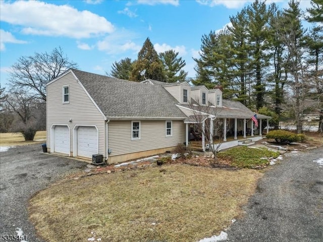 view of front of property with a shingled roof, a porch, central AC unit, a garage, and driveway