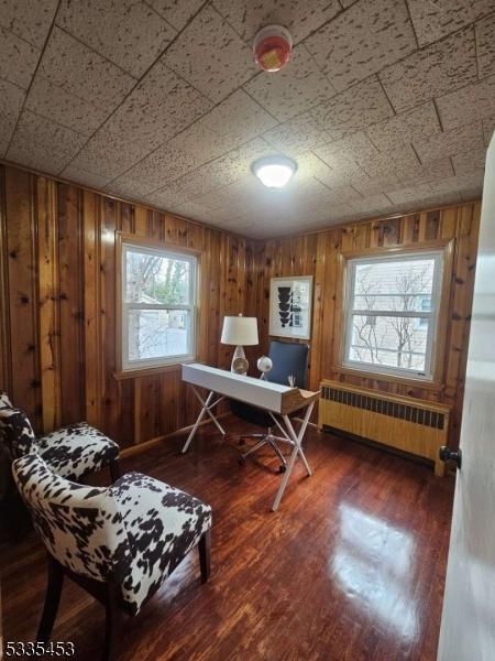 home office featuring dark wood-type flooring, radiator heating unit, and wood walls