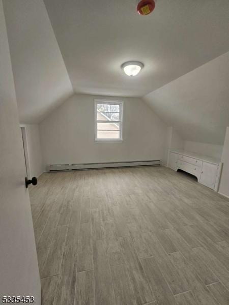 additional living space featuring lofted ceiling, a baseboard radiator, and light wood-type flooring