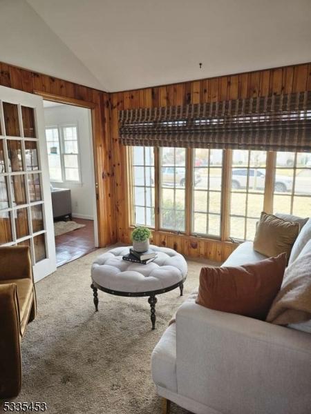 carpeted living room with vaulted ceiling and wooden walls