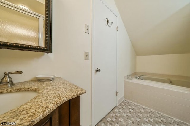 bathroom featuring vanity, vaulted ceiling, and tiled tub