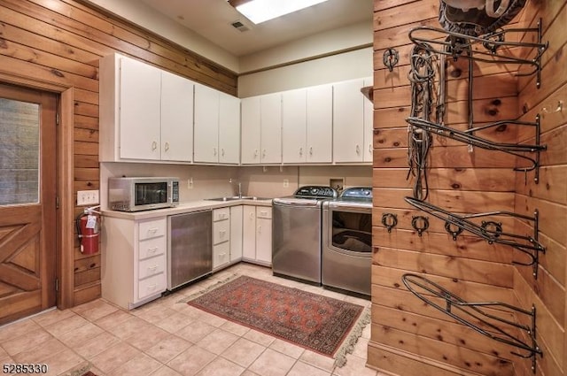 interior space featuring wood walls, white cabinetry, separate washer and dryer, light tile patterned floors, and dishwashing machine