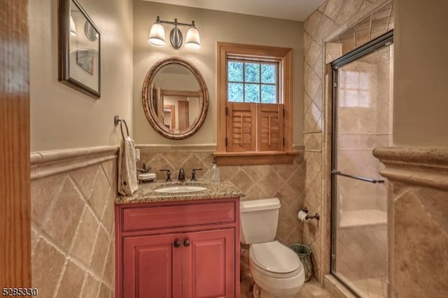 bathroom with vanity, toilet, tile walls, and a shower with shower door