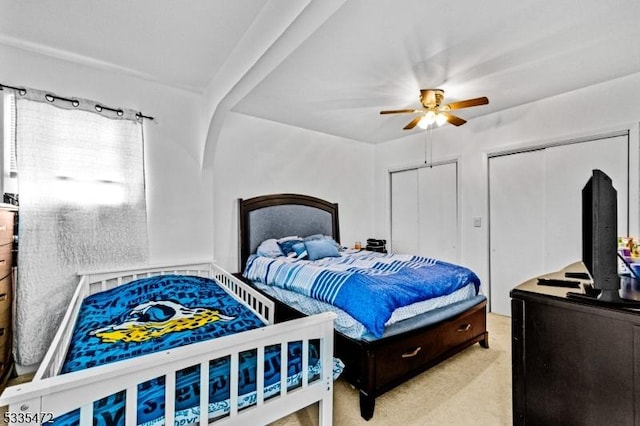 bedroom with multiple closets, light carpet, and ceiling fan