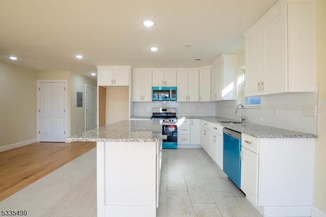 kitchen with sink, light stone counters, appliances with stainless steel finishes, a kitchen island, and white cabinets