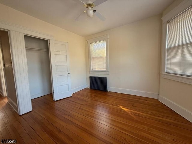 unfurnished bedroom with multiple windows, radiator heating unit, and dark hardwood / wood-style floors