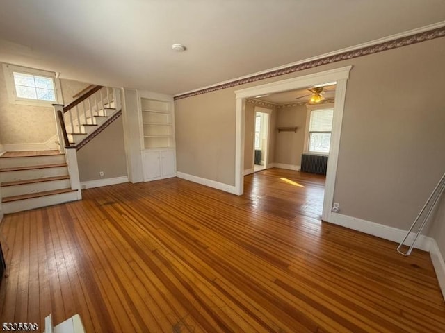 unfurnished living room with crown molding, wood-type flooring, radiator, and built in features