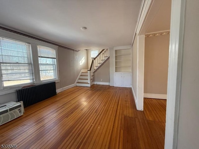 unfurnished living room featuring hardwood / wood-style flooring, radiator, and built in features