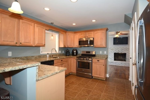 kitchen with decorative light fixtures, sink, light stone counters, stainless steel appliances, and a brick fireplace