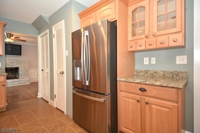 kitchen with stainless steel refrigerator with ice dispenser, light brown cabinetry, light stone counters, a brick fireplace, and ceiling fan