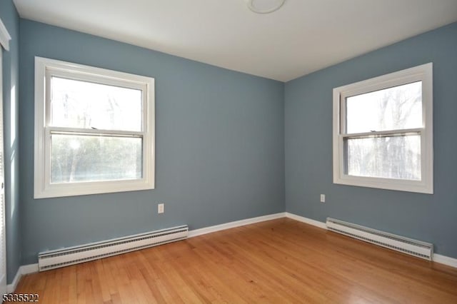 empty room with a baseboard radiator, a healthy amount of sunlight, and light hardwood / wood-style flooring