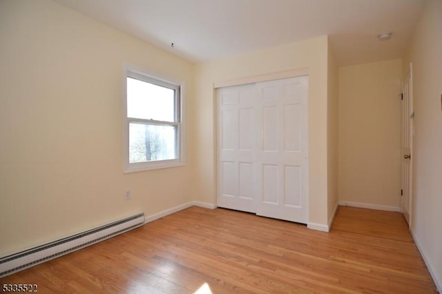 unfurnished bedroom with light hardwood / wood-style flooring, a baseboard radiator, and a closet