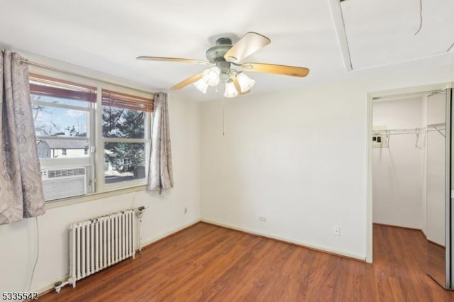 unfurnished bedroom featuring a spacious closet, radiator heating unit, dark hardwood / wood-style floors, a closet, and ceiling fan