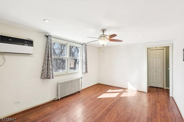 unfurnished room featuring hardwood / wood-style flooring, an AC wall unit, radiator, and ceiling fan